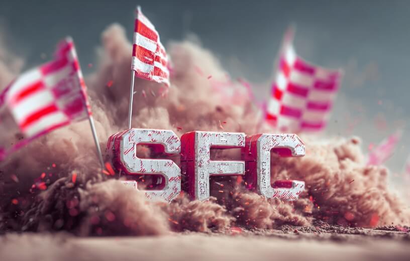 Large block letters spelling 'SFC' stand amidst a swirling cloud of brown dust and confetti. Several red and white striped flags are planted in the ground around the letters.